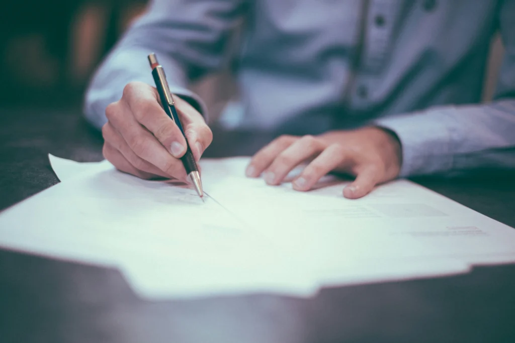 Business owner signing paperwork with a pen during a professional service agreement review.